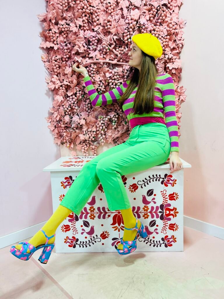 girl in colorful clothes sitting on  a bench, pink leaves in the background
